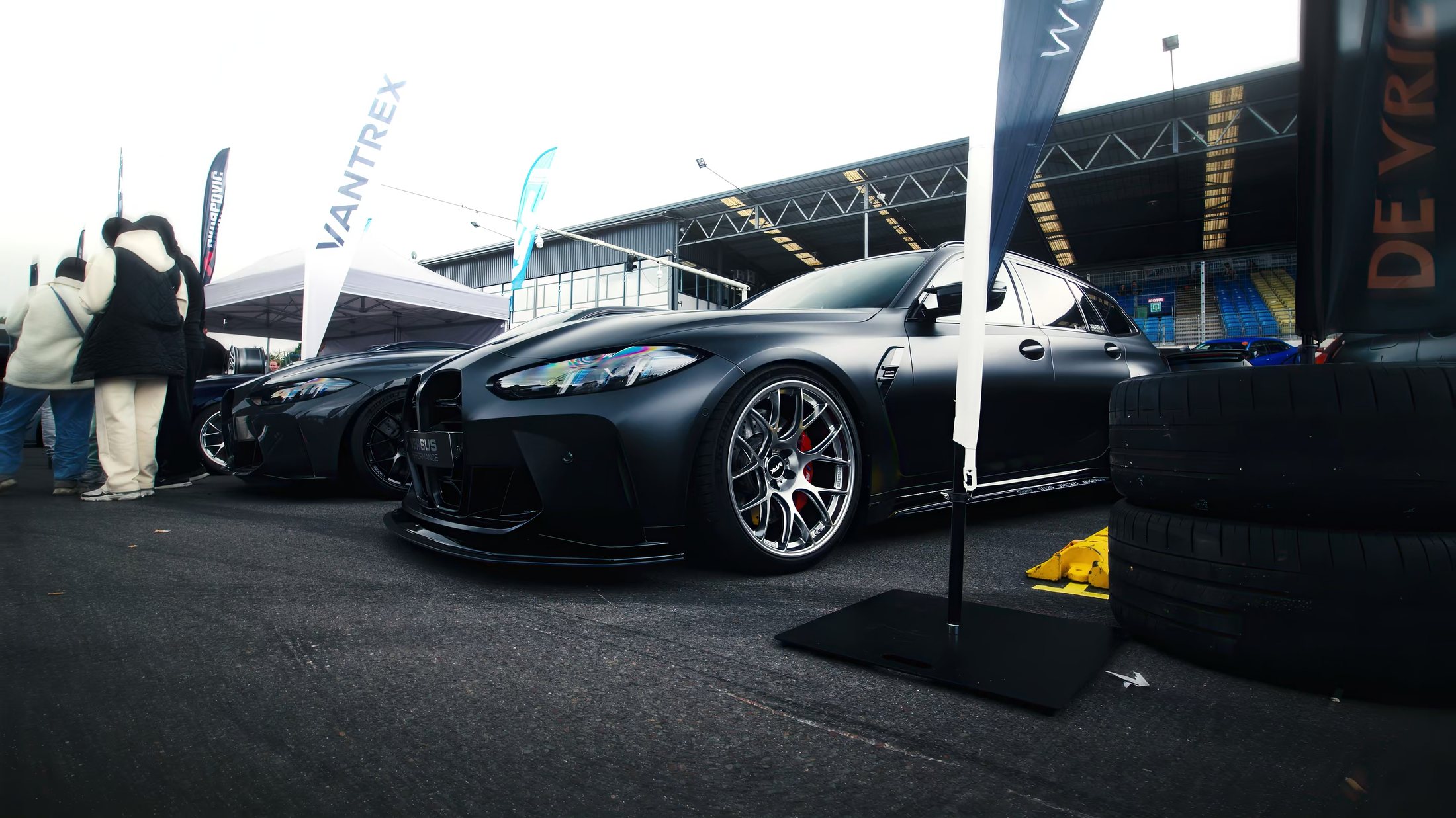 Zwarte BMW M3 Touring op de pitstraat van Bimmerfest, met bandenstapel en vlaggen