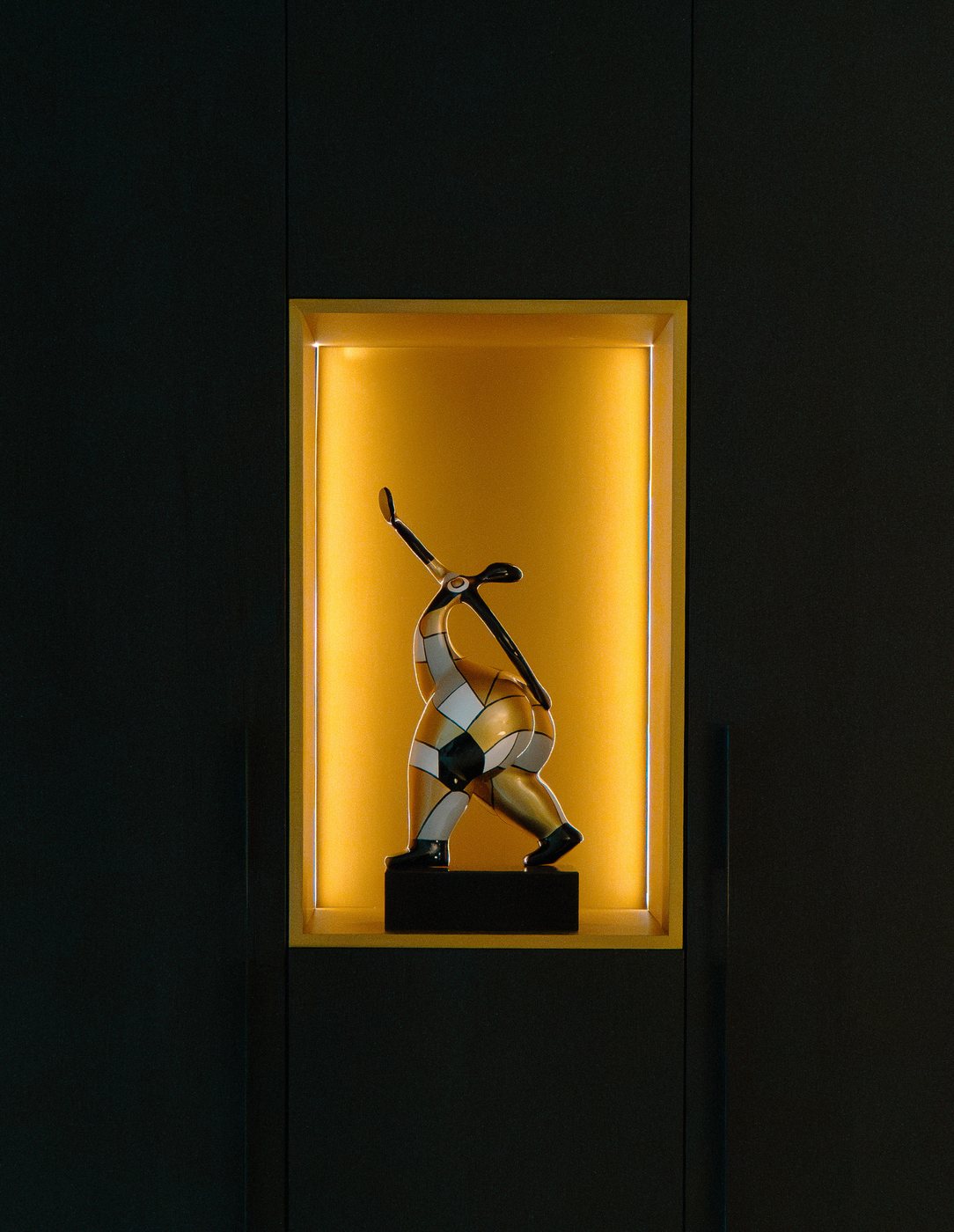 Verlichte gouden nis met een beeldje in een donkere kastenwand