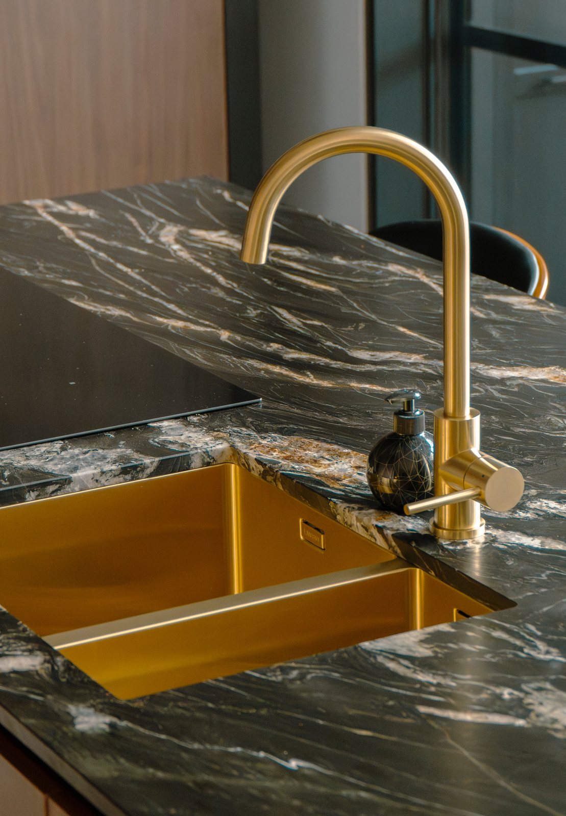 Keukeneiland in donker marmer met een gouden kraan en gouden spoelbak