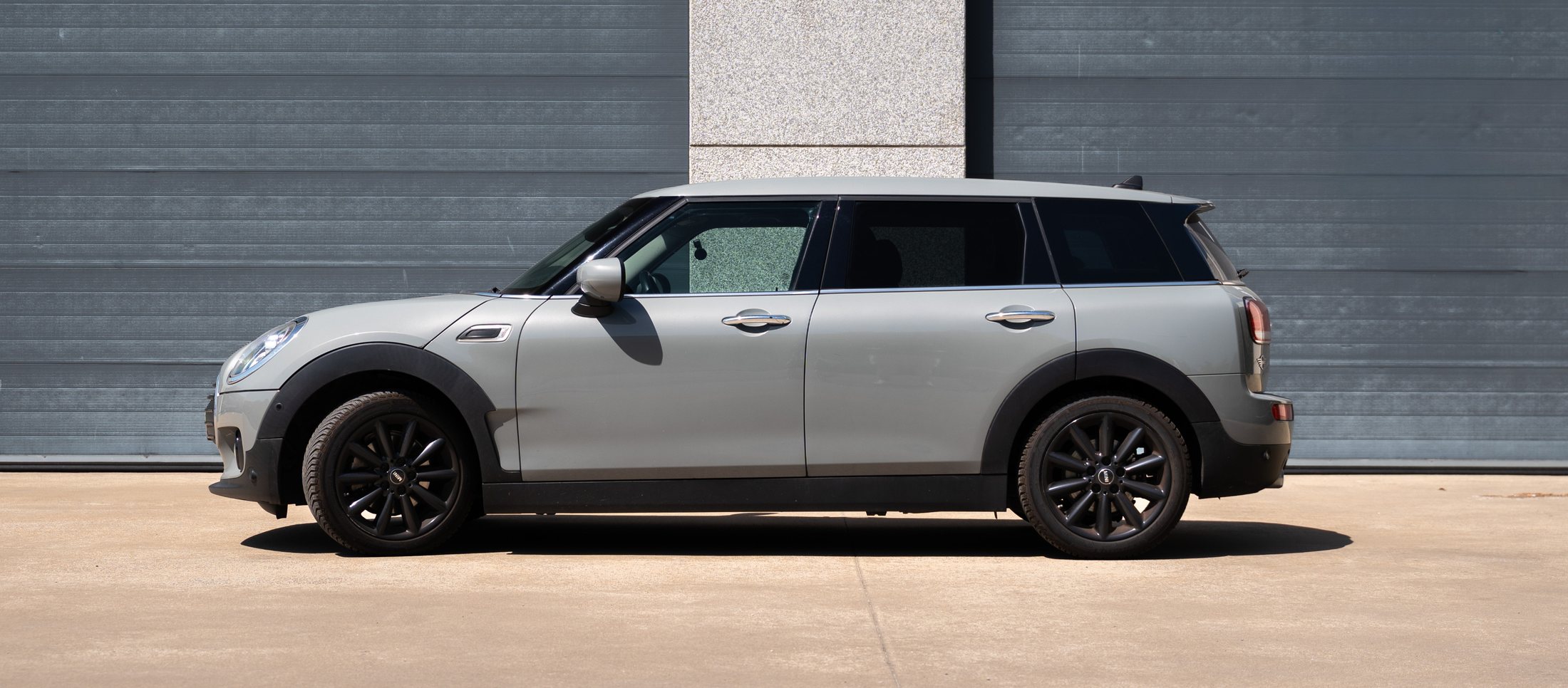 Grijze Mini Clubman van opzij voor een grijze garagepoort
