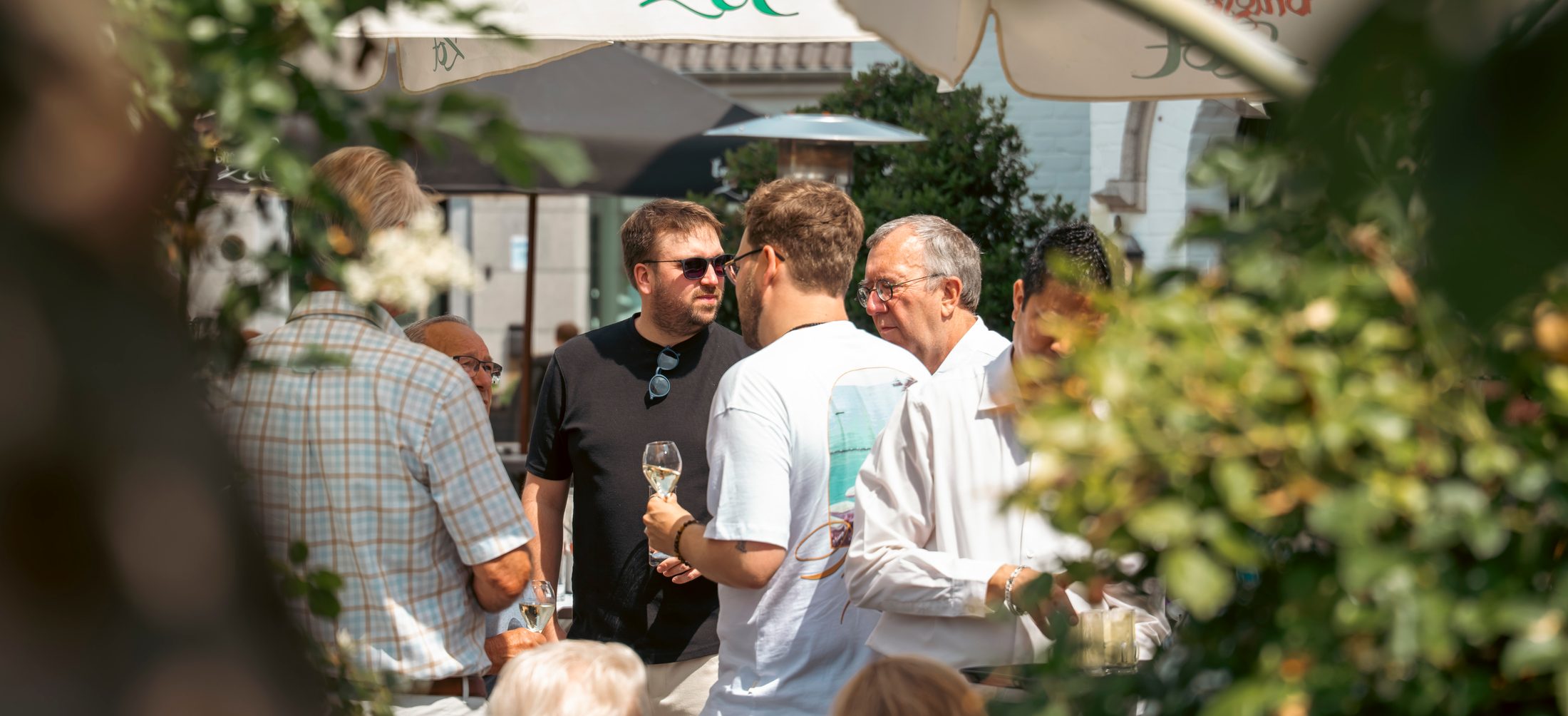 Gasten met een glas wijn in gesprek op een zonnig terras