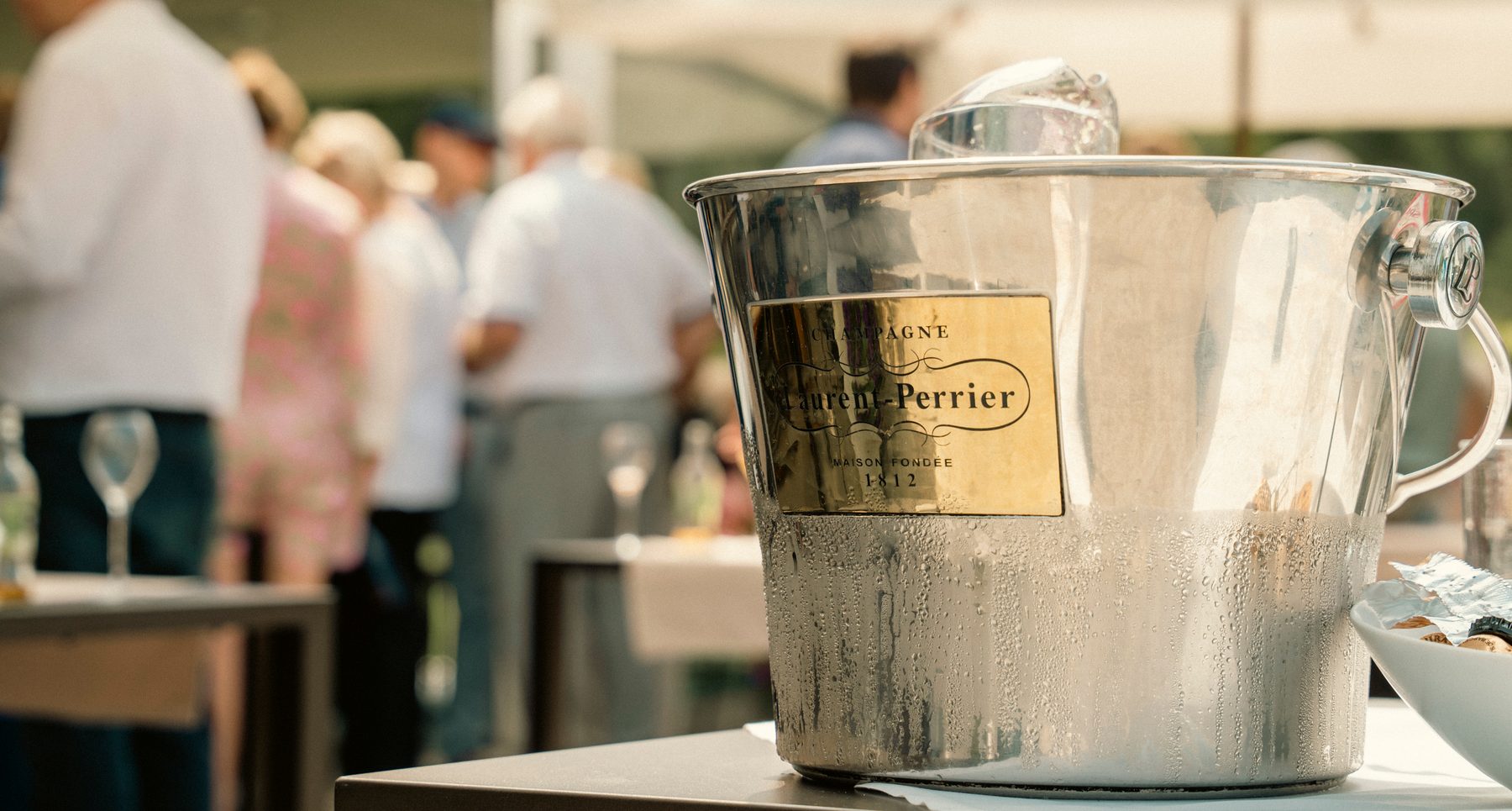 Zilveren Laurent-Perrier champagne-emmer op een tafel, met gasten op de achtergrond